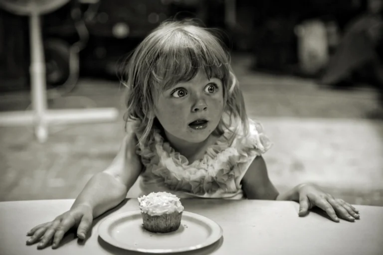 Kind sitzt an einem Tisch mit einem Cupcake auf einem Teller in einem unscharfen Hintergrund.