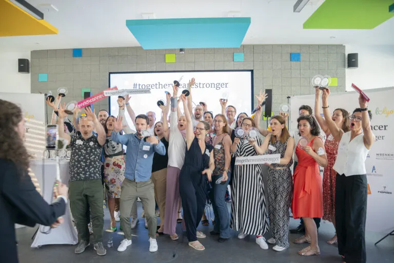 Gruppe von Menschen auf einer Bühne feiert mit Trophäen und Schildern vor einer Leinwand mit dem Hashtag #togetherwearestronger