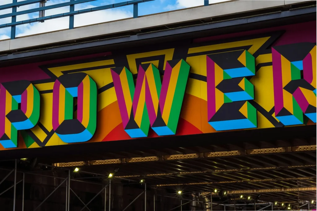 Bunte Wandgestaltung mit großem Schriftzug ‚POWER‘ in kräftigen Farben unter einer Brücke