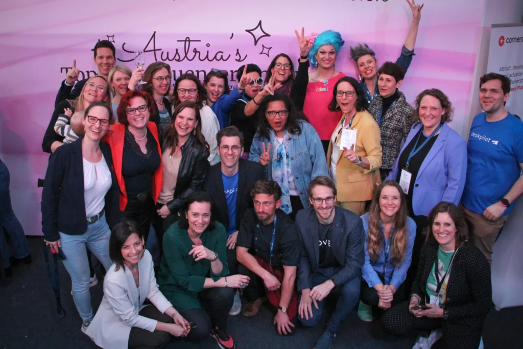 Eine Gruppe von Menschen, HR Expert*innen, jubeln vor der Leinwand Austria's Top HR Influencer*innen.