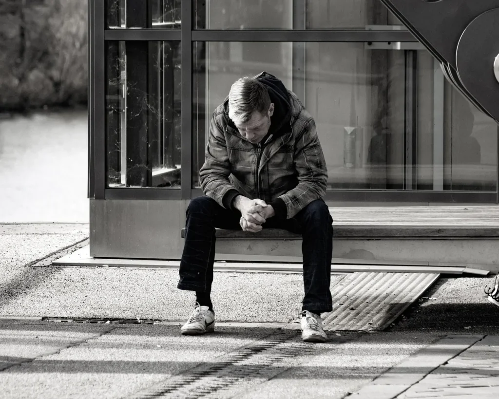 Person sitzt allein auf einer Bank in einer urbanen Umgebung – Symbol für Isolation und die Bedeutung von Prävention