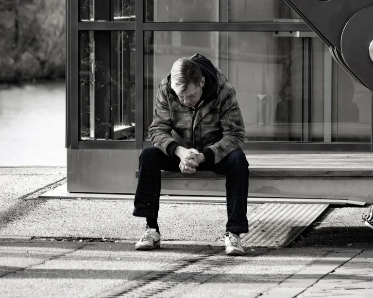 Person sitzt allein auf einer Bank in einer urbanen Umgebung – Symbol für Isolation und die Bedeutung von Prävention