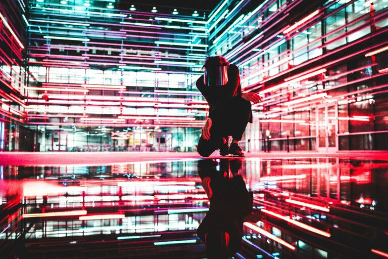 Eine Person in futuristischer Umgebung mit neonfarbenen Lichtlinien, umgeben von reflektierenden Flächen in einem technisch anmutenden Raum.
