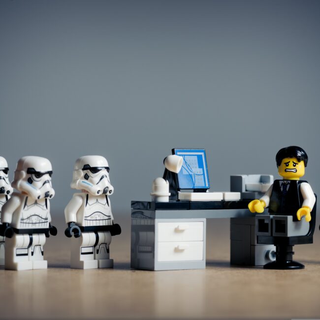 Standardisierte Bewerbungsprozesse im Recruiting symbolisch dargestellt mit Lego‑Figuren vor einem Schreibtisch