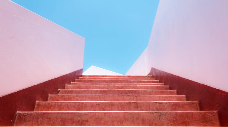 Rote Treppe führt nach oben zu blauem Himmel als Symbol für persönliche Entwicklung und Zukunft der Arbeit